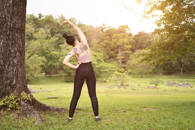 Tatuaje asiático joven haciendo yoga en el parque