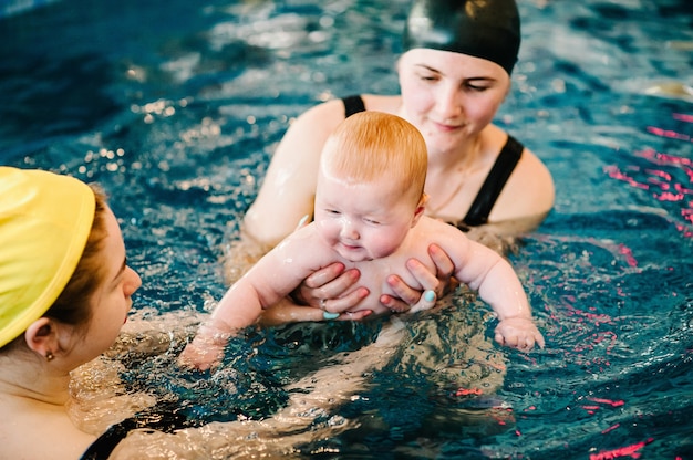 Tauchbaby im Planschbecken. Junge Mutter, Schwimmlehrerin und glückliches kleines Mädchen im Pool. Lernen Sie Kleinkind schwimmen. Genießen Sie den ersten Tag im Wasser schwimmen. Mutter hält Baby und taucht