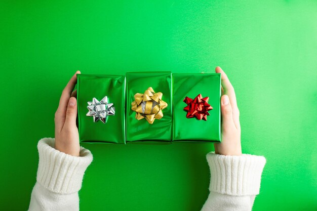 Tauchen Sie in die Weihnachtsmagie, erste Persönlichkeit von oben, die Hände greifen nach einer üppigen grünen und silbernen Geschenkkiste mit einem Bogen auf grünem Hintergrund, perfekt für den Muttertag.