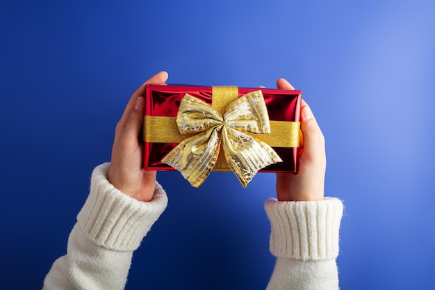 Tauchen Sie in die Weihnachtsmagie Erstpersönlichkeitsansicht von oben der Hände greifen Sie nach einer üppigen roten Geschenkkiste mit Bandbogen auf blauem Hintergrund Perfekt für Valentinstag MarketingxA