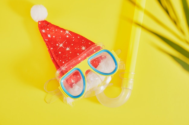 Tauchset, weihnachtsmannmütze und palmblatt auf gelbem hintergrund, weihnachtsferien am strand in einem warmen land