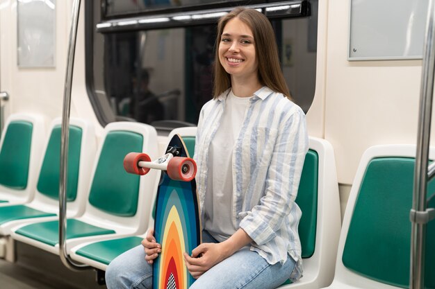 Tausendjährige Frau mit Longboard in der U-Bahn sitzend lächelnd in die Kamera städtisches Hobby