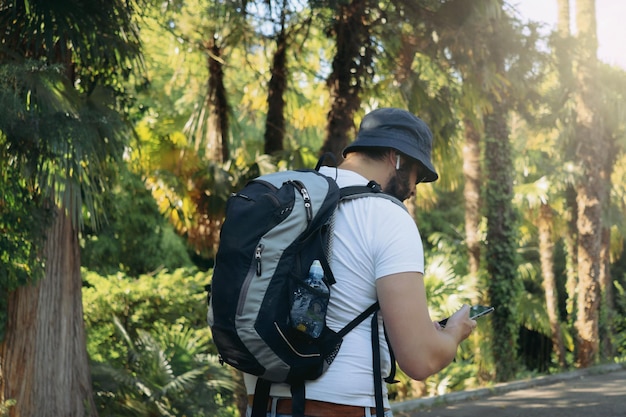 Tausendjähriger bärtiger Touristenmann mit Eimerhut, Rucksack und Ohrstöpseln, der sein Smartphone benutzt