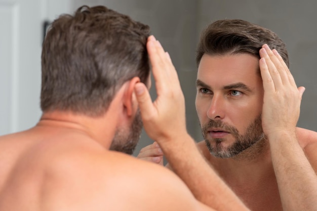 Tausendjähriger hispanischer Mann, der in Spiegelgesichtshaut und Stoppeln schaut, männliches Schönheitspflegeprodukt Hautpflege