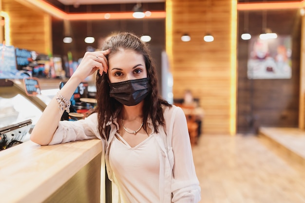 Foto taxa de quarentena em um café, uma jovem com uma máscara preta. foto de alta qualidade