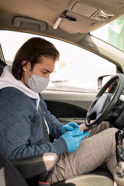 Taxifahrer mittleren Alters in Stoffmaske und Handschuhen, die während der Fahrt mit der mobilen App arbeiten