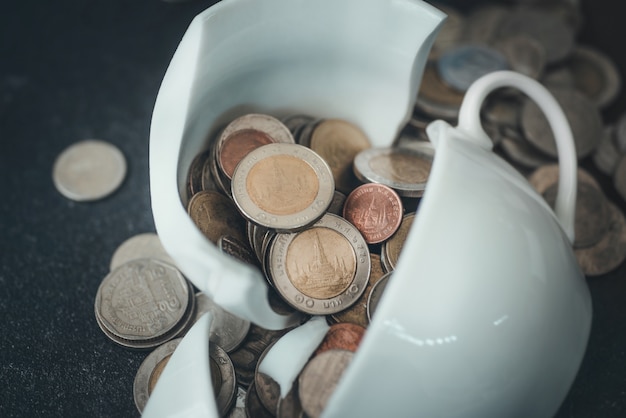 La taza acaba de romperse en pedazos y el dinero de la moneda está tirado a su alrededor.