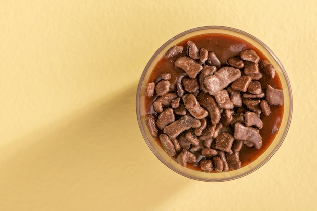 Taza de acrílico con brigadeiro y chispitas de chocolate sobre fondo amarillo