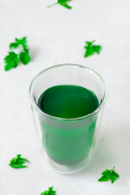 Taza con agua de clorofila sobre fondo gris neutro con imagen vertical de hojas verdes