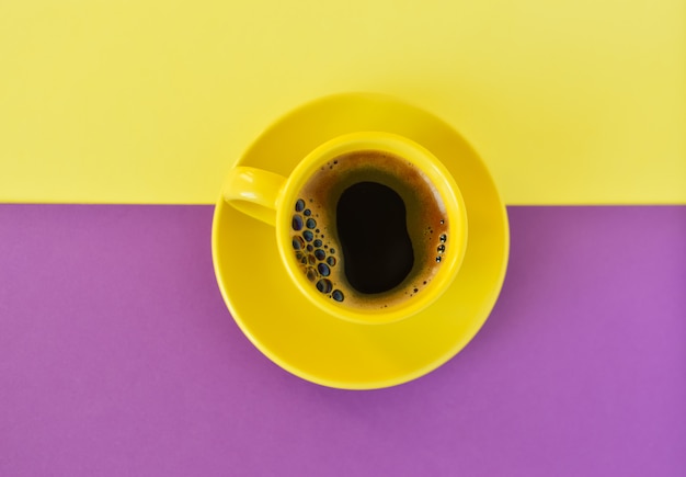 Taza amarilla con café sobre un fondo amarillo y violeta doble