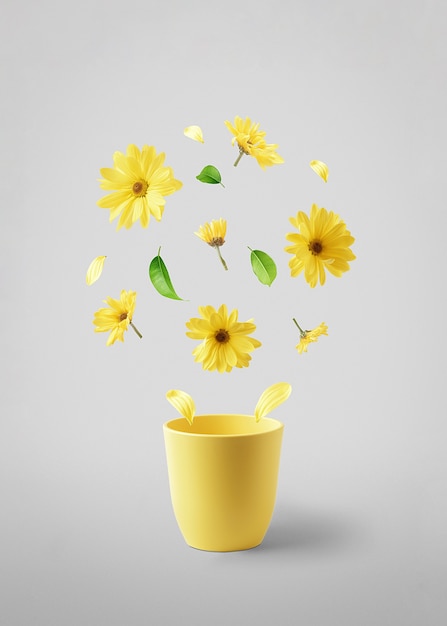 Taza amarilla con flores amarillas voladoras sobre una mesa gris. El concepto de primavera.