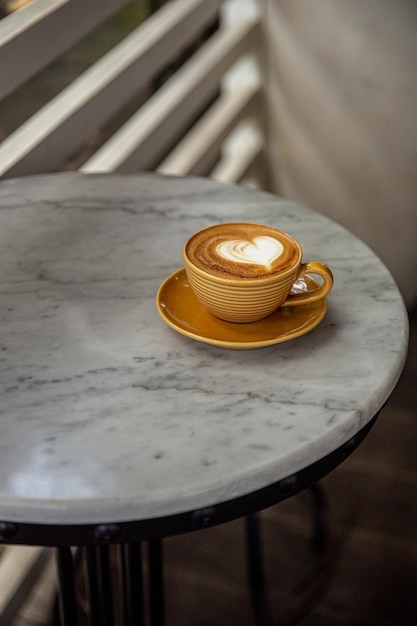 Taza amarilla de moda de capuchino caliente sobre fondo de mesa de mármol Arte latte en forma de corazón para símbolo de amor