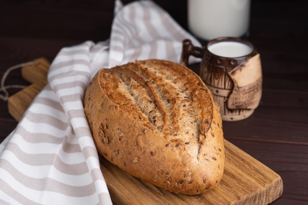 Taza de arcilla de cebolla de racimo de pan de centeno de cereales caseros frescos y una botella de leche en una tabla de cortar de madera