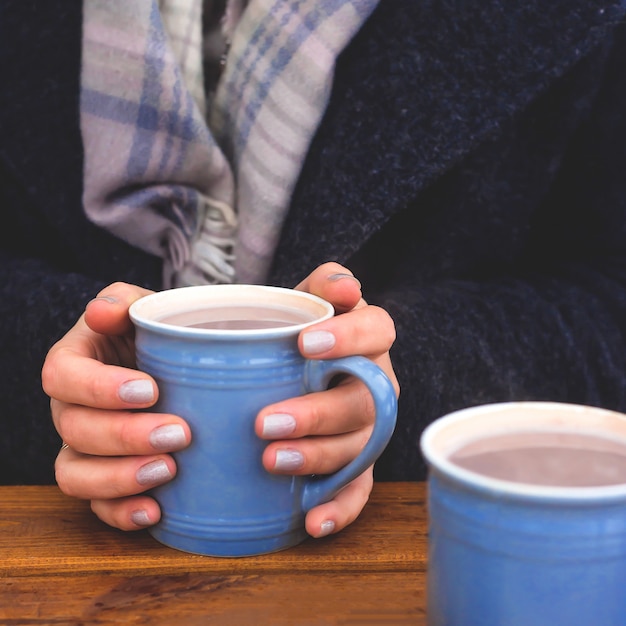 Taza azul de cacao en manos femeninas en la mesa de terraza de invierno.