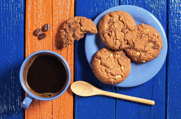 Taza azul de café caliente con deliciosas galletas de chocolate en la mesa de madera colorida, vista superior