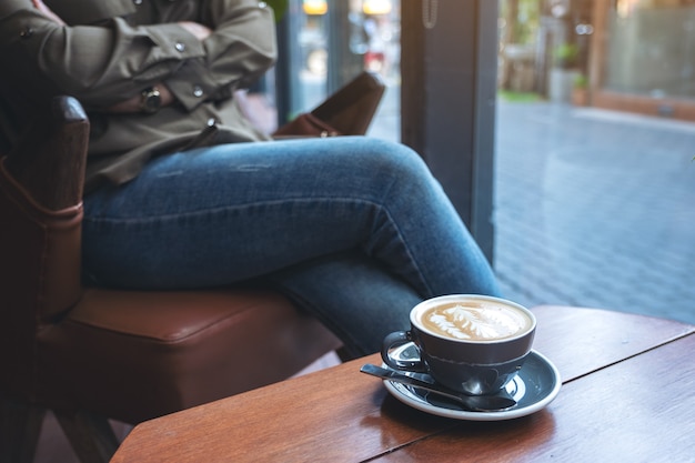 Taza azul de café con leche caliente en la mesa de madera con una mujer sentada en el café