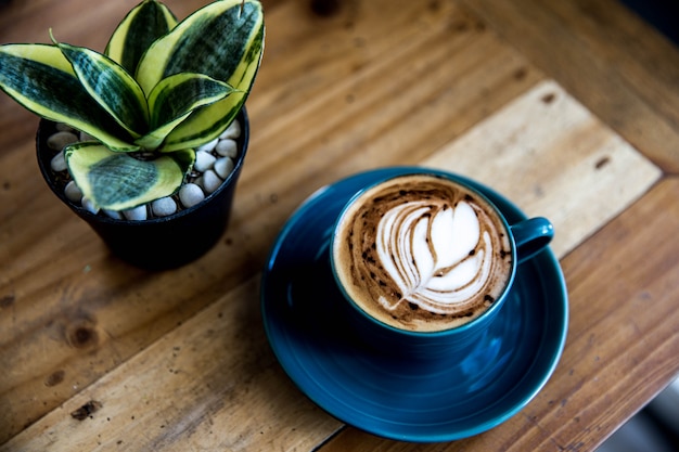 Taza azul de capuchino caliente está sobre la mesa de madera