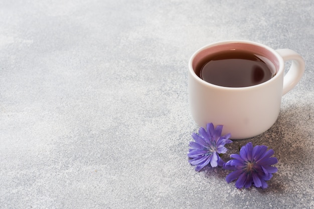 Taza con bebida de achicoria y flores de achicoria azul en mesa gris