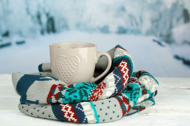 Taza de bebida caliente con bufanda caliente en la mesa