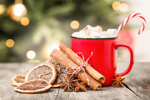 Una taza con una bebida caliente malvaviscos bastón de caramelo y especias en el fondo del árbol de Navidad