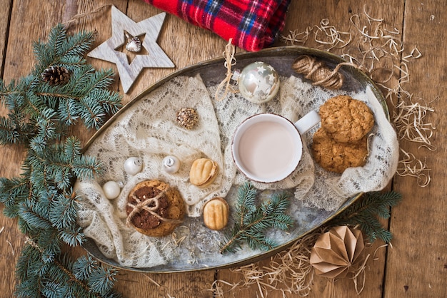 Taza con bebida y galletas con decoración navideña.