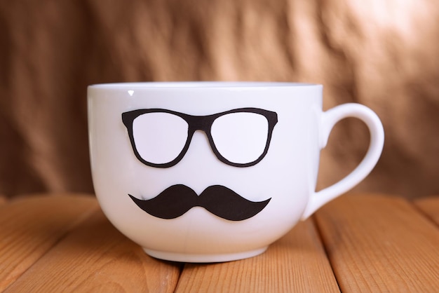 Taza con bigote en la mesa sobre fondo marrón