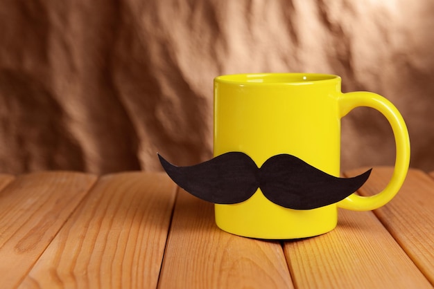 Taza con bigote en la mesa sobre fondo marrón