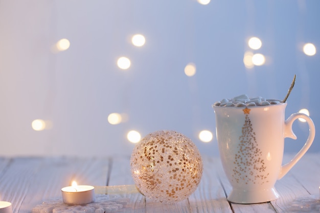 Taza blanca con adornos navideños dorados sobre mesa de madera blanca