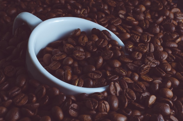 Taza blanca ahogada en granos de café tostados, foto tonificada