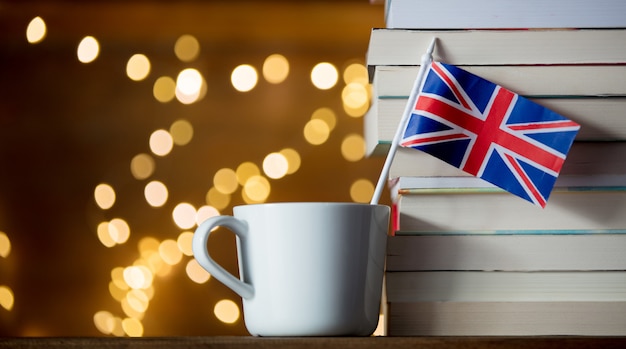 Taza blanca y bandera de Gran Bretaña cerca de pila de libros