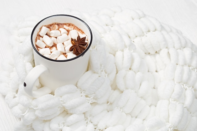 Taza blanca de bebida de chocolate caliente con malvaviscos y anís sobre tela blanca esponjosa
