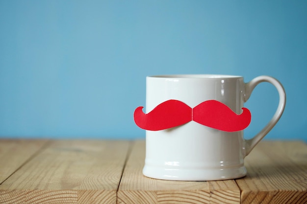Una taza blanca con un bigote de papel rojo felicitaciones o un regalo para papá
