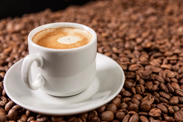 taza blanca con café aromático sobre granos dispersos.