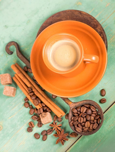 Taza blanca de café caliente con espuma de leche, canela, anís estrellado y granos de café en la mesa de madera