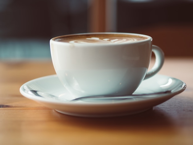 Foto la taza blanca de café caliente sirvió en la tabla de madera en el café.