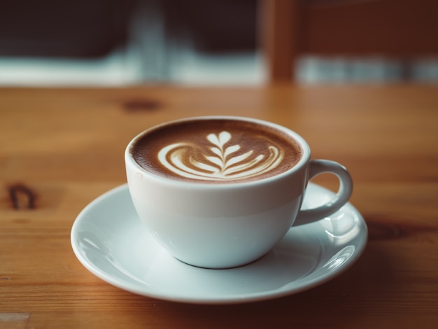 La taza blanca de café caliente sirvió en la tabla de madera en el café.