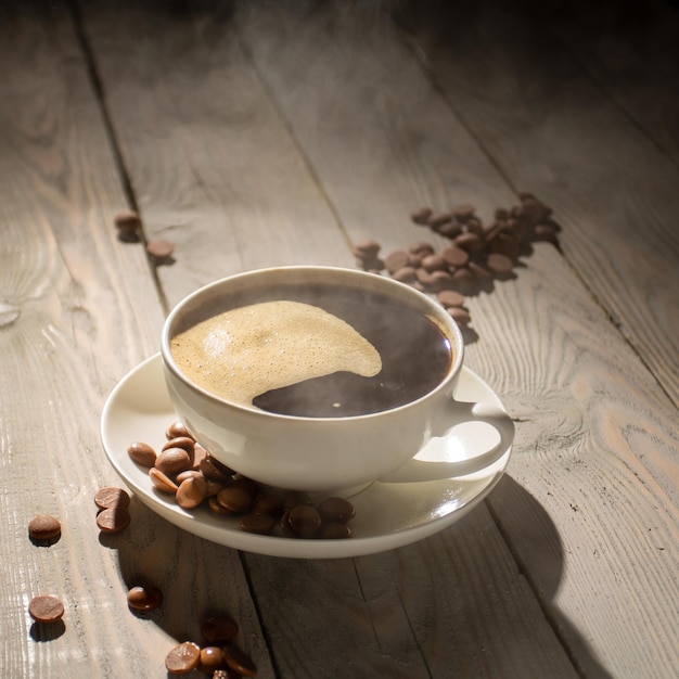 Taza blanca de café caliente con vapor sobre una mesa de madera retroiluminada