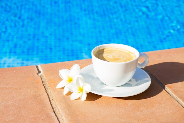 Taza blanca de café cerca del agua de la piscina