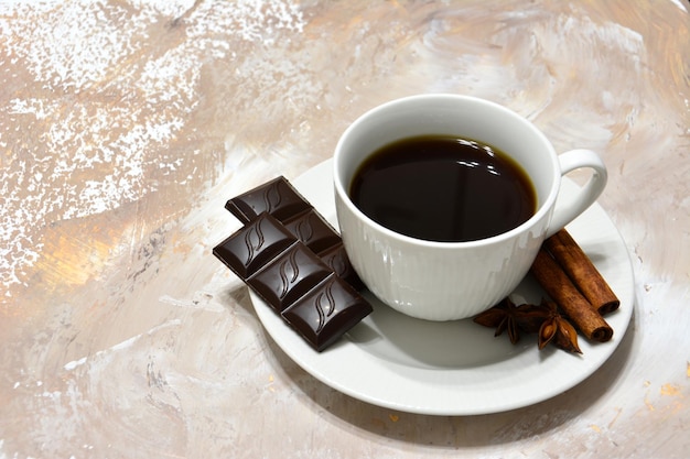 taza blanca de café con chocolate, canela y badian sobre fondo beige