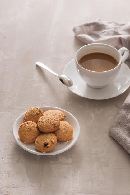 Taza blanca de café cremoso con galletas de mantequilla sobre fondo blanco.