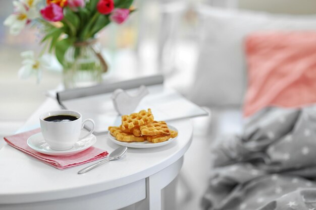 Taza blanca de café y dulces en una mesa de madera en una habitación luminosa