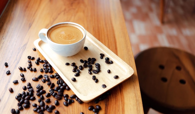 Taza blanca de café espresso y granos de café tostados en un mostrador de madera en la cafetería