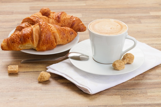 Taza blanca con café expreso recién hecho con agua y croissant