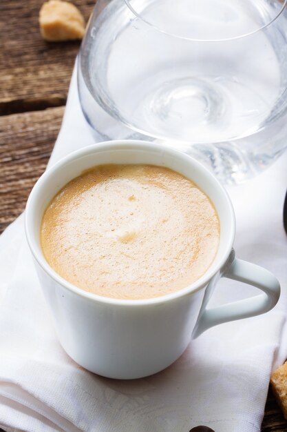 Taza blanca con café expreso recién hecho y vaso de agua