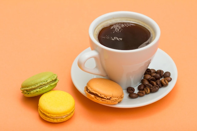 Taza blanca de café con granos de café y deliciosos pasteles macarons de diferentes colores