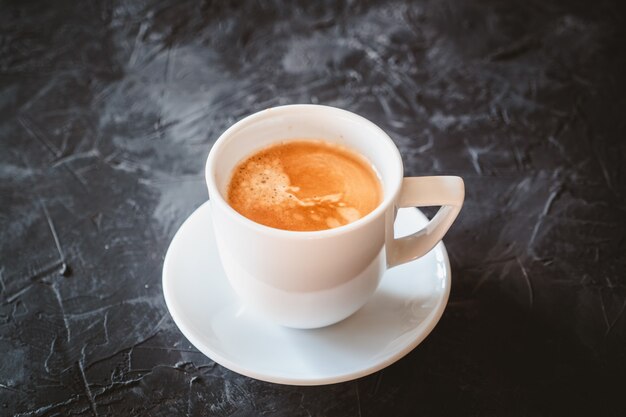 Taza blanca de café con leche en una mesa de pizarra negra