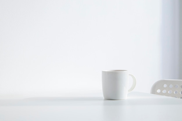 Taza blanca con café en una mesa blanca bajo luz natural