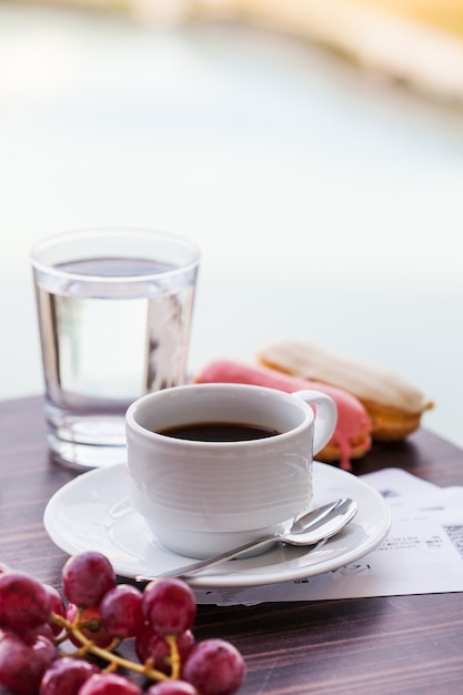 Taza blanca con café negro con canutillos y un vaso de agua potable