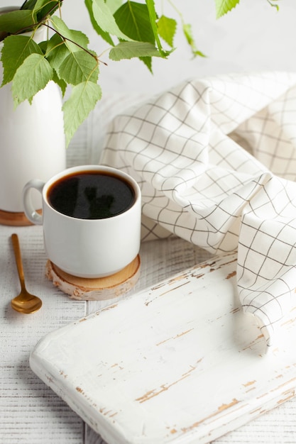 Una taza blanca con café negro una rama con verde deja un tablero vacío un lugar para insertar su produ ...