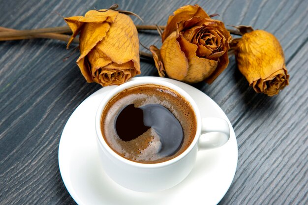 Taza blanca con café negro y rosa seca.